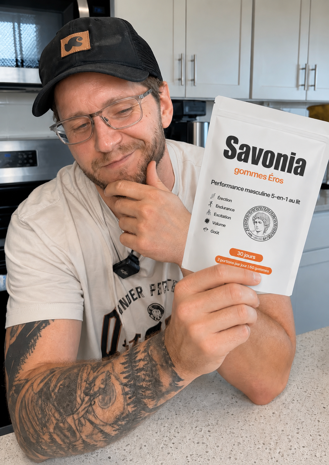 A man with glasses and tattoos holds a white pouch of Savonia Eros Gummies in a kitchen.